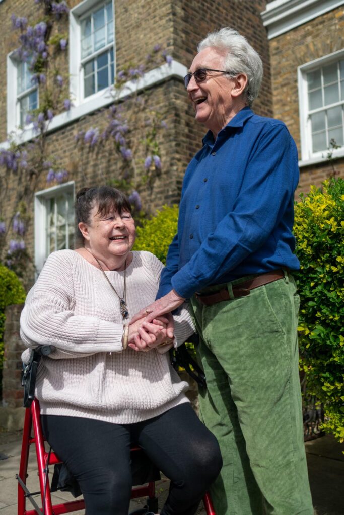 An elderly couple embracing outside their house, sharing a loving moment
