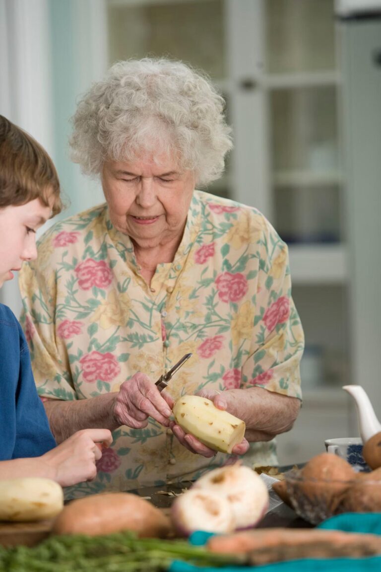 An elderly woman peeling potatoes alongside her grandson in a warm, well-lit kitchen, symbolizing family bonding and healthy living.