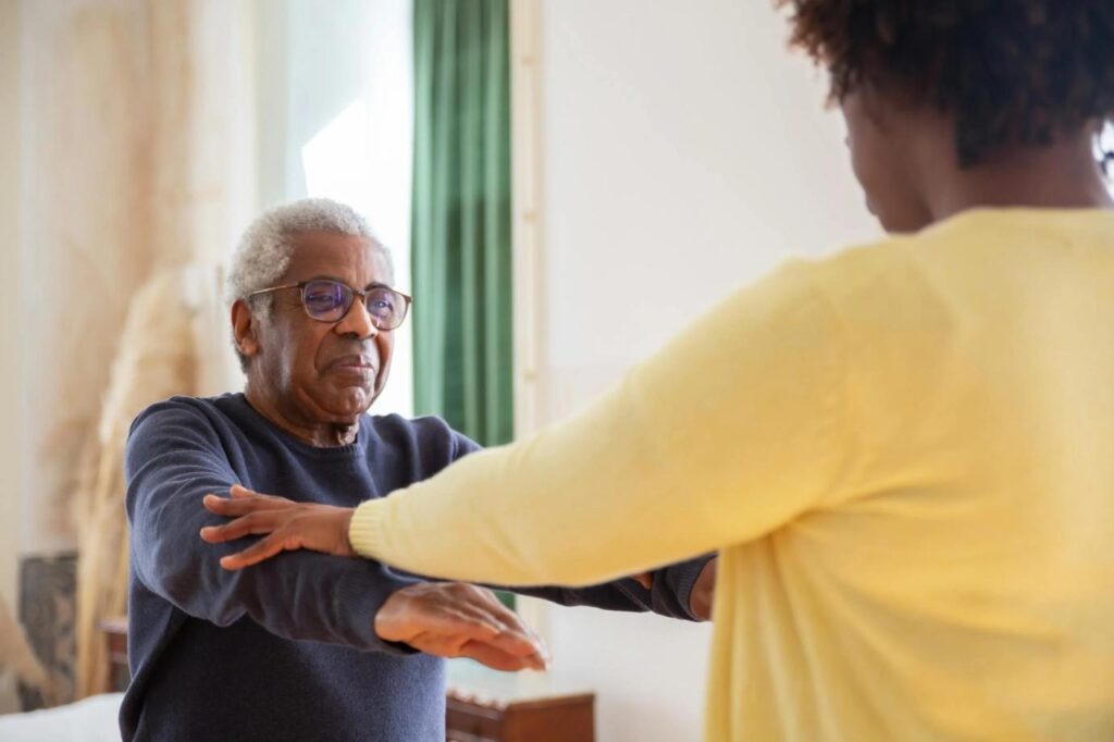 An elderly man receiving physical therapy at home, guided by a therapist.