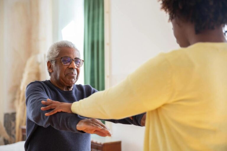 An elderly man receiving physical therapy at home, guided by a therapist.