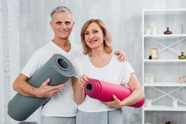 A couple standing in a gym holding exercise mats and smiling at the camera.