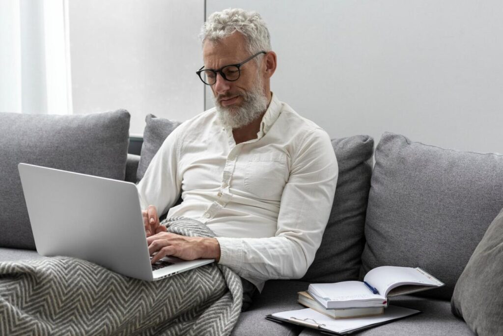 A senior man using a laptop while sitting on a couch at home.