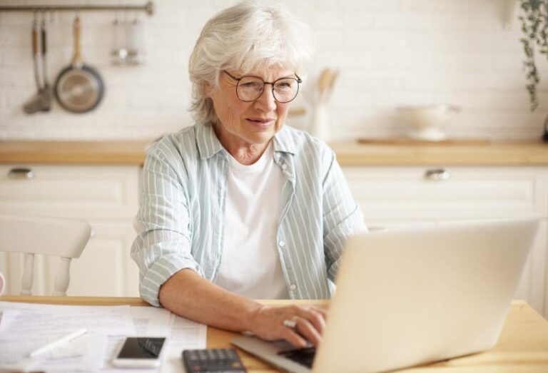 An excited elderly woman looking at a laptop.