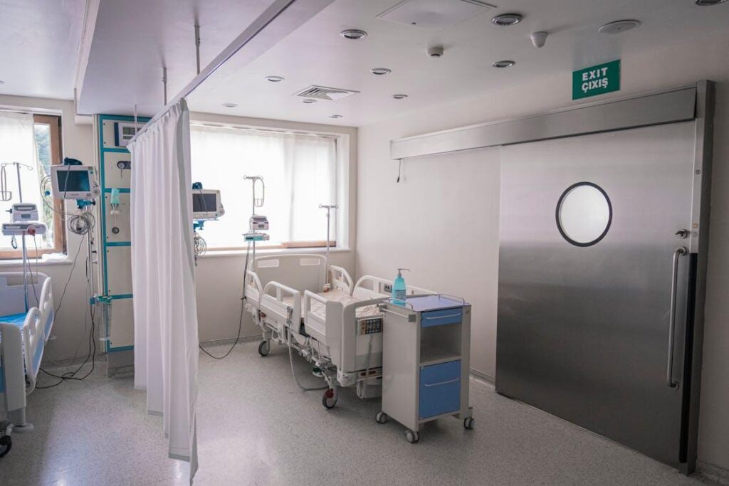 an empty hospital bed next to the exit door inside a hospital room