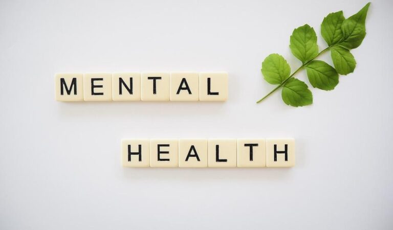Scrabble tiles spelling out “mental health” with a leaf placed next to them