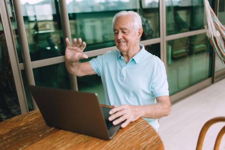 A retiree smiles while using his laptop.