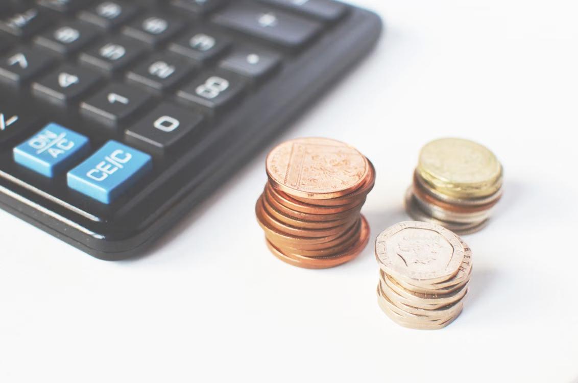 Stacked coins next to a calculator on a desk.