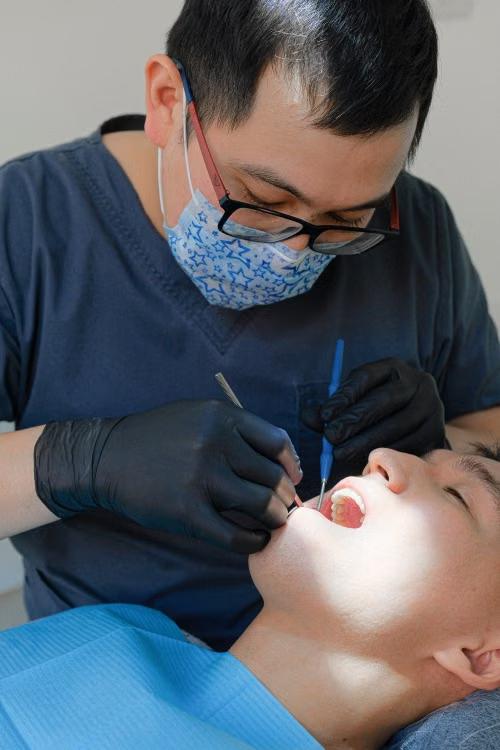 A dentist examines a patient's teeth using dental tools in a clinic.