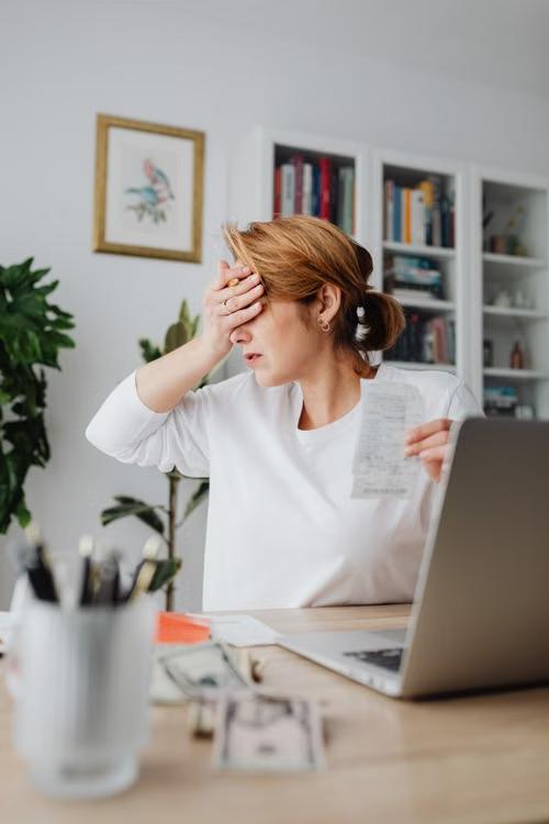 A woman reviews a receipt while sitting in front of a laptop.