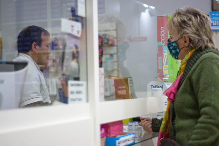 A woman speaks with a pharmacist behind the pharmacy counter.